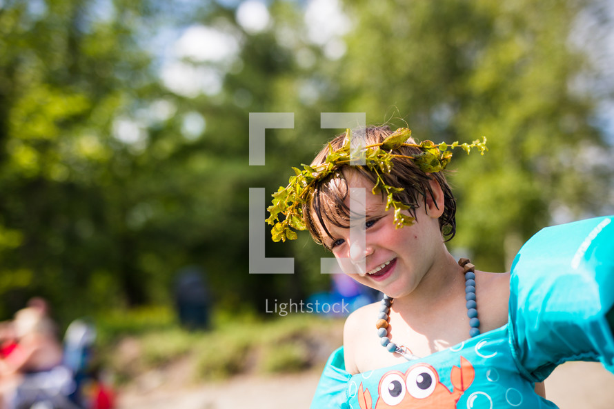 a child in a floatie playing at a lake with a crown of leaves in his hair 