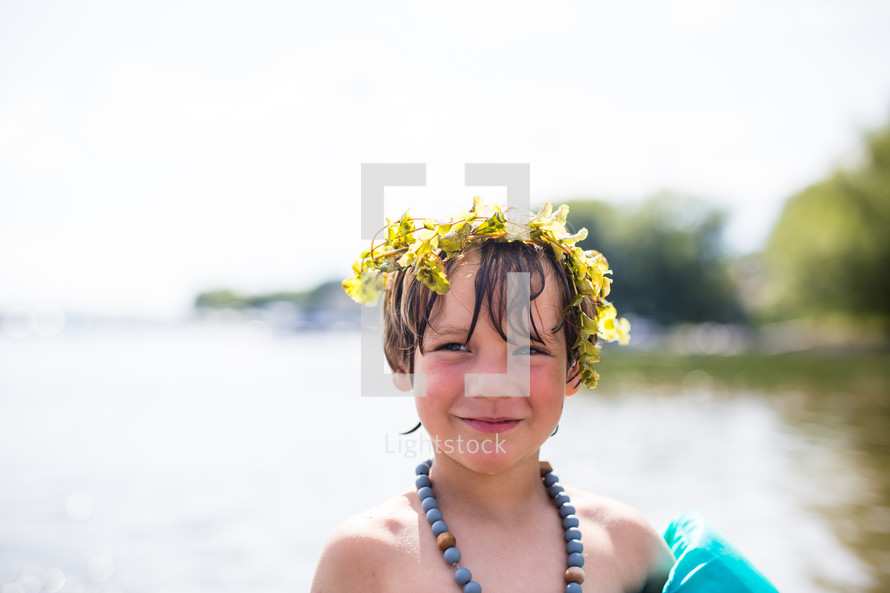 a child in a floatie playing at a lake and a crown of leaves 