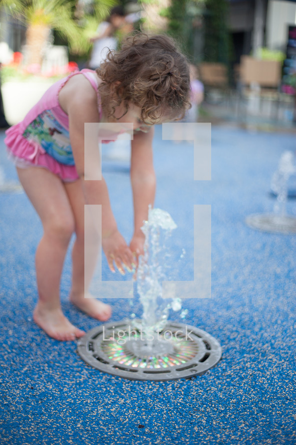 toddler girl in a bathing suit playing in a fountain at a splash pad  