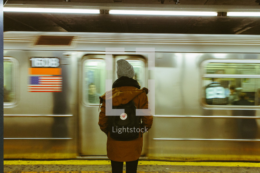woman standing in a subway in front of a passing subway train 