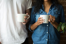 A man and woman standing and holding coffee cups.
