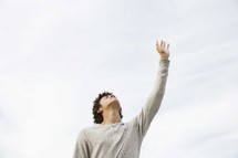 teen boy with eyes closed and his hand raised in praise.