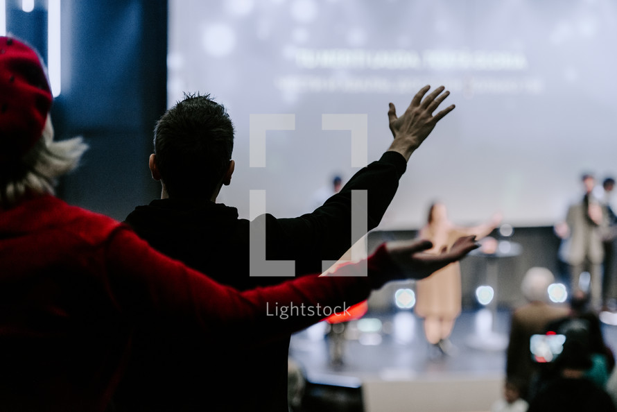 Behind view of a man and woman's hands raised in the air during worship at a church service.