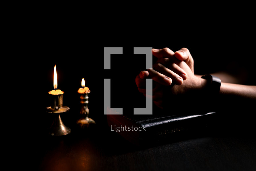 Bible and candlelight with praying hands