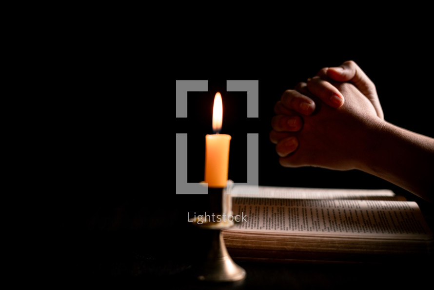 Bible and candlelight with praying hands