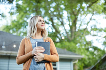 a woman standing outdoors clasping a Bible 