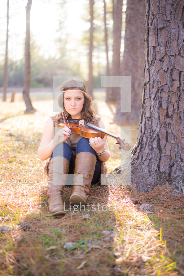 young woman sitting on the forest floor with a violin