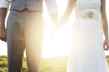 Newly married bride and groom holding hands under intense sunlight.
