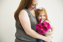 A mother hugs her little girl and holds a bouquet of flowers.