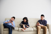 siblings using electronics on a couch 