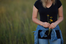 a young woman standing in a field of tall grass holding flowers 