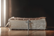 silver cross leaning against a Bible spine 