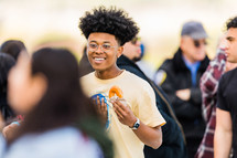 A smiling young man eating a donut in a group of people.