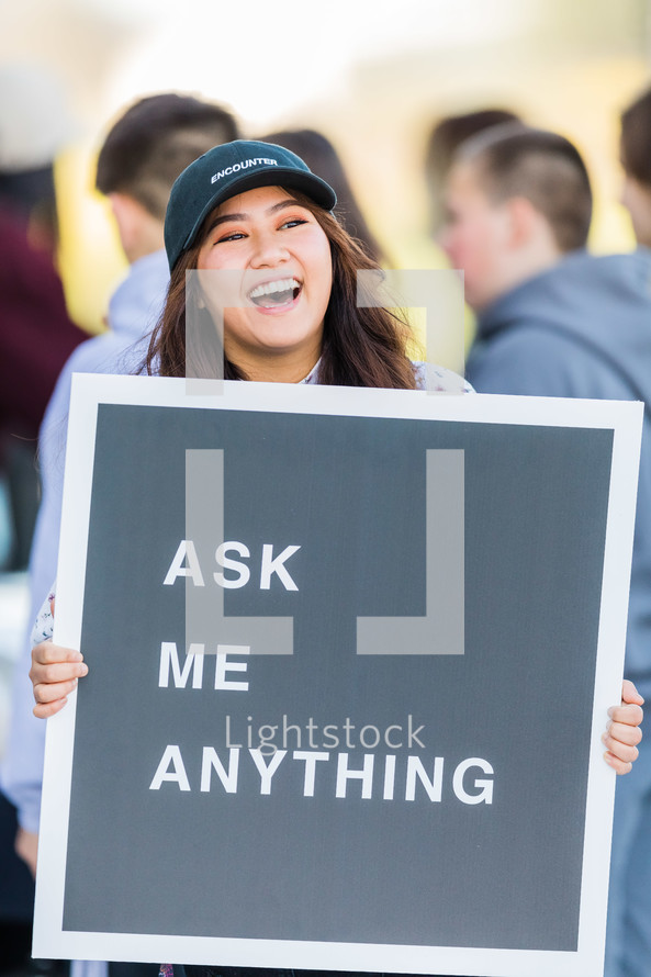 A laughing woman holding a sign reading, "Ask Me Anything."