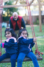 A grandfather pushing his granddaughters on a swing 