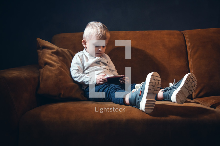 Handsome Little Rich Boy with Smartphone Sitting in Dark Interior