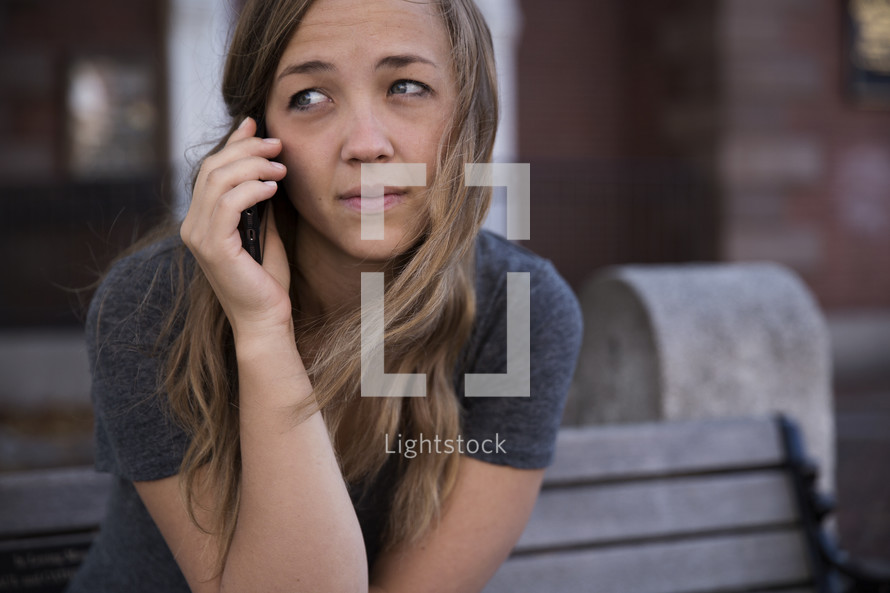 a young woman on the phone sitting on a park bench 