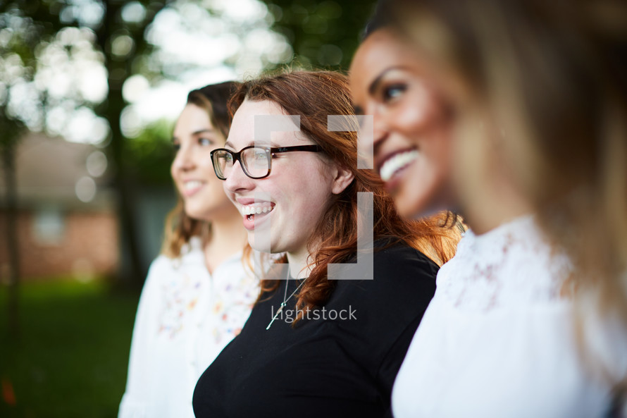 faces of a group of women standing outdoors in a row 