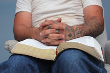 tattooed hands praying on a Bible 