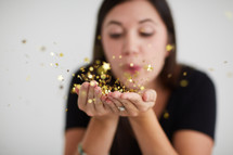 a woman blowing gold confetti 