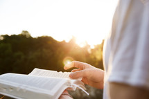 a woman turning the pages of a Bible outdoors in sunlight 