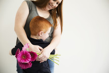 A woman hugs her son and holds a bouquet of flowers.