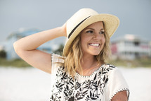 Smiling woman in a hat standing outside on the beach.