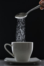 ea cup or coffee and pouring sugar spoon on black background