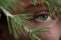 eyes of a woman looking through pine branches 