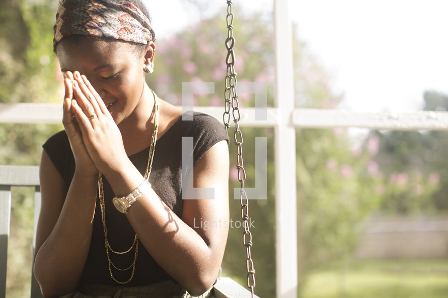 Woman sitting outside on a porch swing praying.