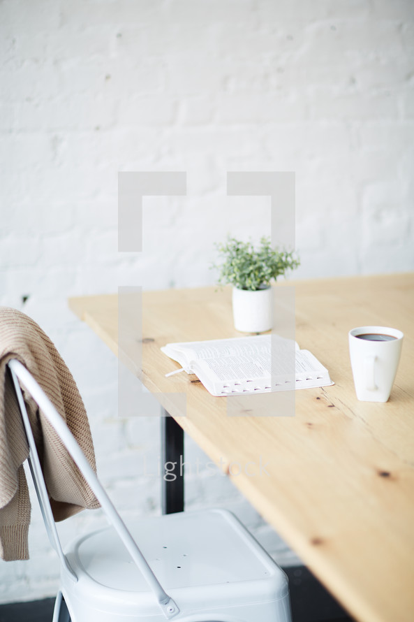 a Bible on a wood table, sweater, and coffee mug 