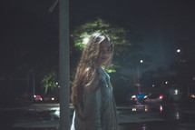 a girl standing in a parking lot at night 