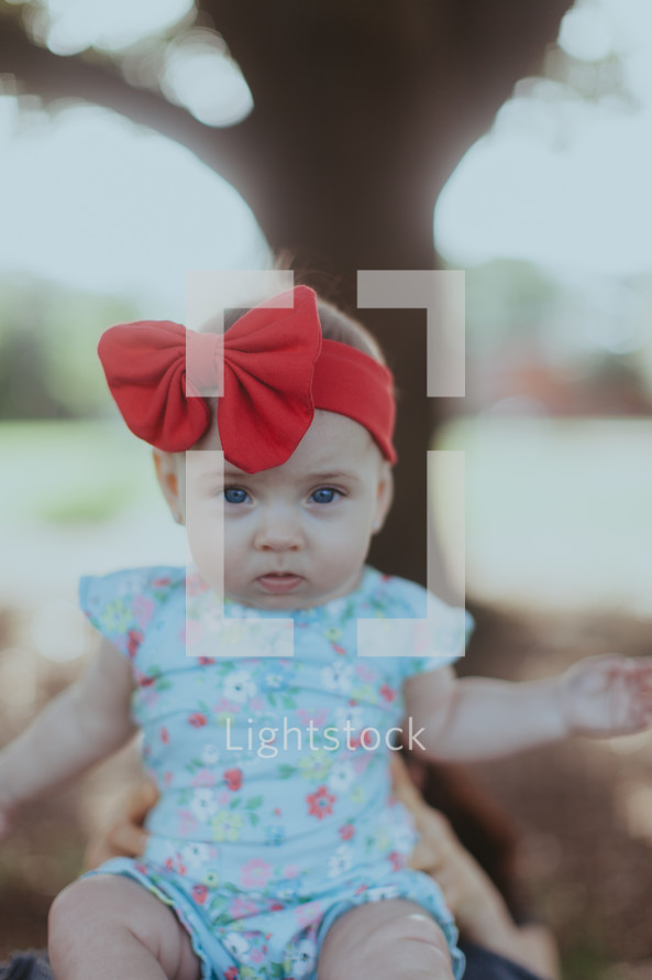 an infant girl in a red headband and bow
