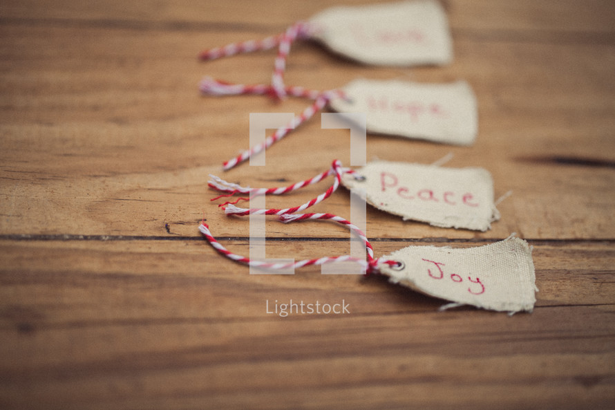 Christmas gift tags lined up with "Joy" being in the front, on a wood grain background.