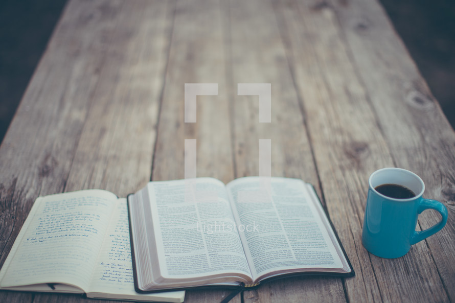 open Bible, journal, and coffee mug on a wood table 