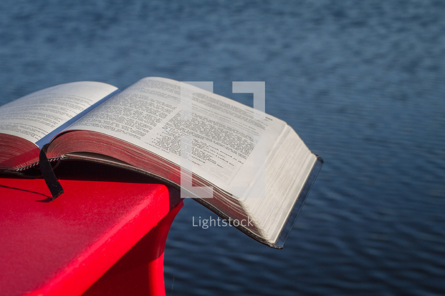 Bible on a Muskoka chair with a lake in the background.