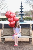 teen girl holding heart shaped red balloons 