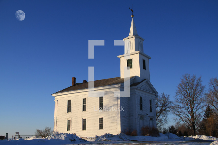 white church and steeple surrounded by snow and a full moon overhead