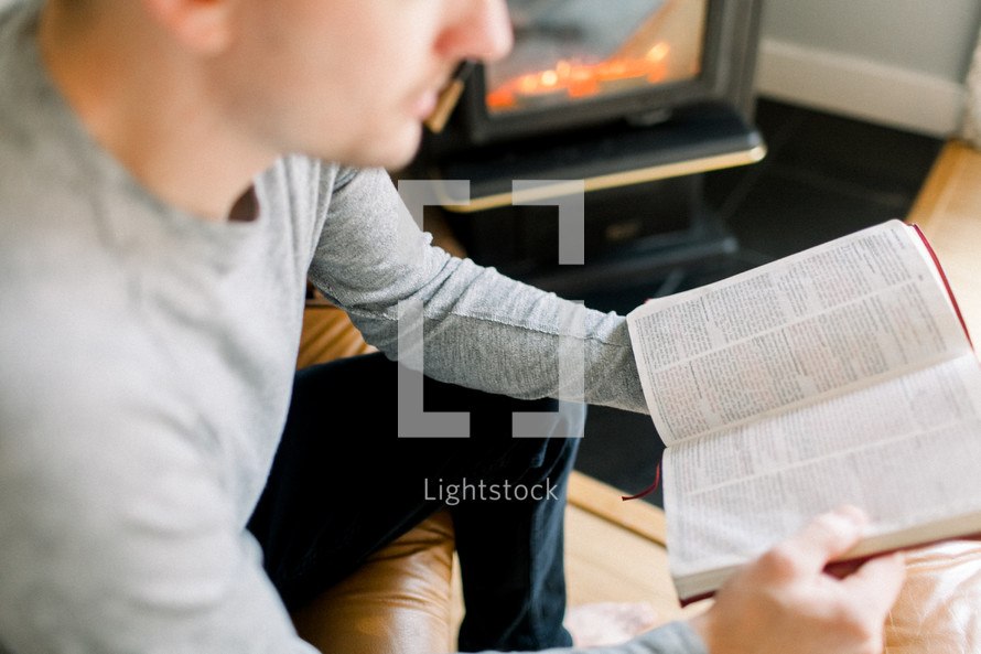 a man reading a Bible by a fireplace 