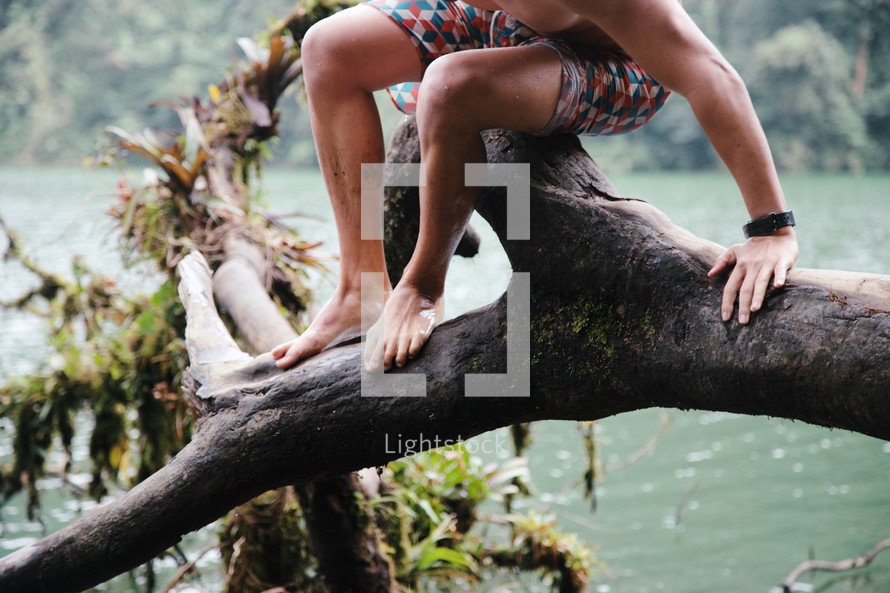 man sitting on a fallen tree hanging over a lake 