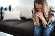 a woman sitting on a couch praying 