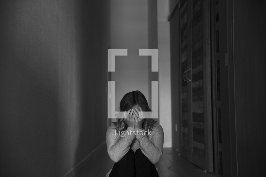 a woman sitting alone in a hallway covering her face with her hands 