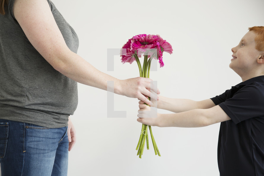 A little boy gives his mother a bouquet of pink flowers.
