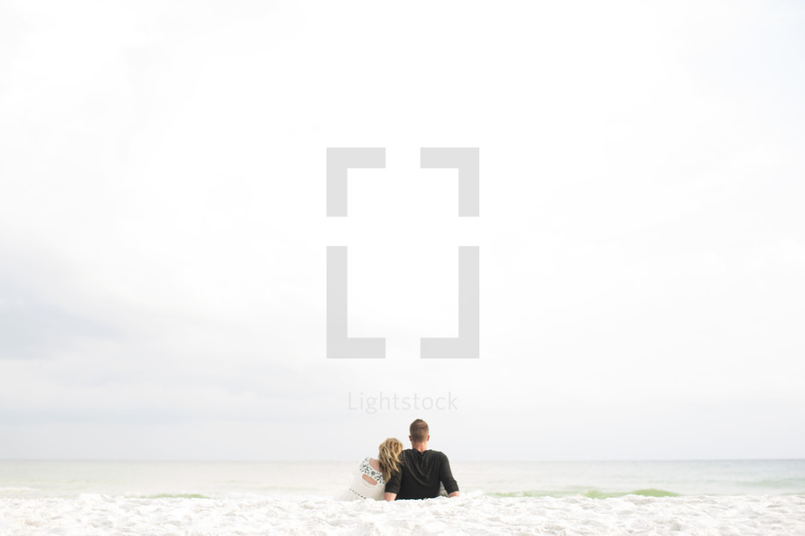 couple sitting on a beach in the sand snuggling 