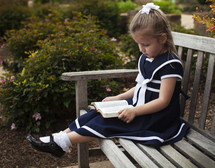 Girl sitting on a park bench reading the Bible.