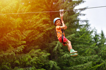 kid with helmet and harness on zip line between trees