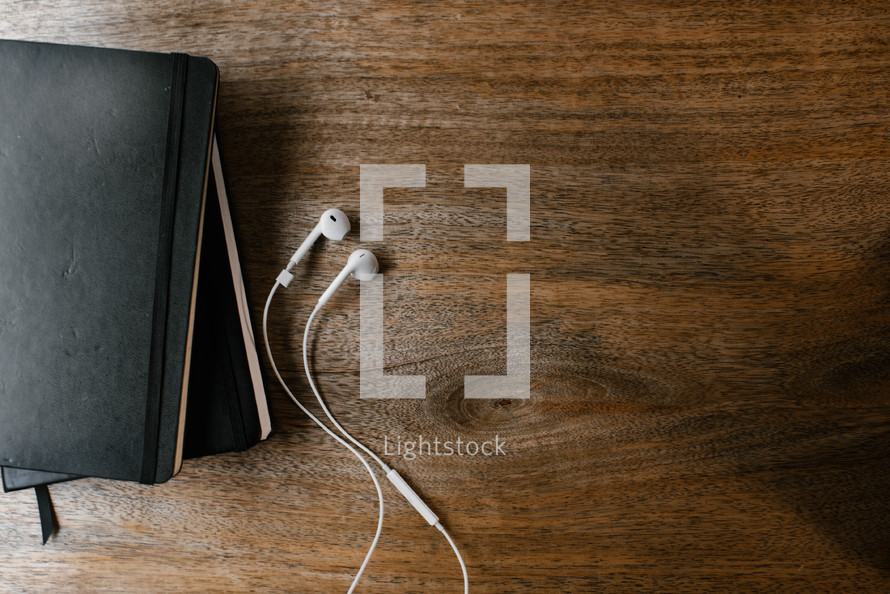 Bible, journal, and earbuds on a wood desk 