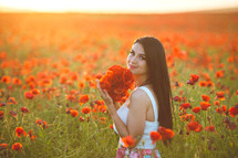 a woman picking flowers in a field a field of red poppies 