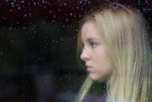 side profile of a woman's face through a rainy window 
