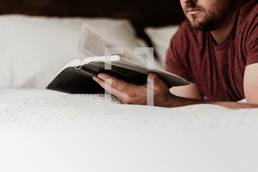 man lying on a bed reading a Bible 